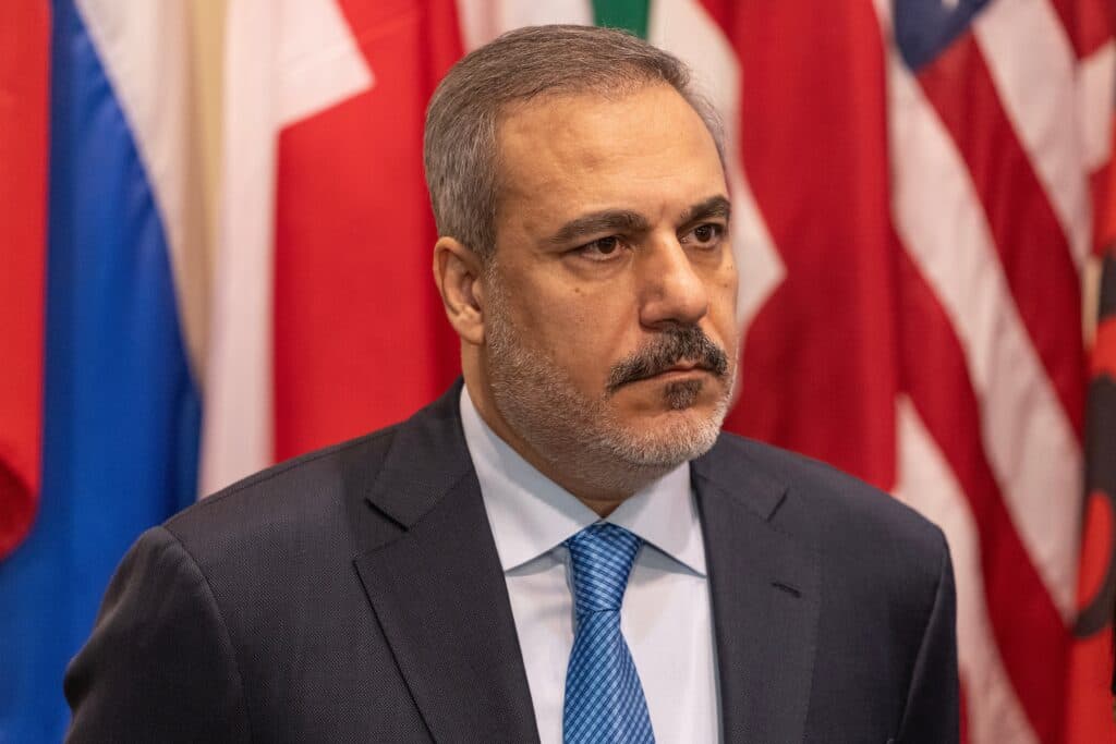 Turkish Foreign Minister Hakan Fidan sits in front of Turkish and international flags.