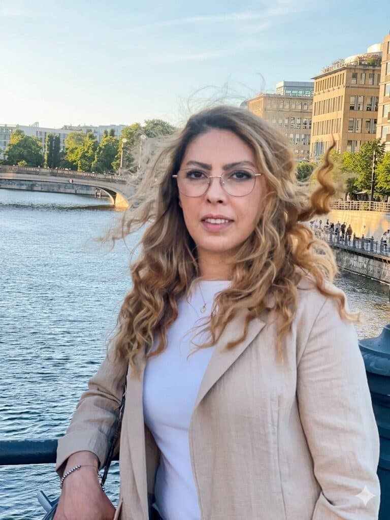 Zaharia, an independent Iranian journalist living in Germany, stands by the water in an urban setting.