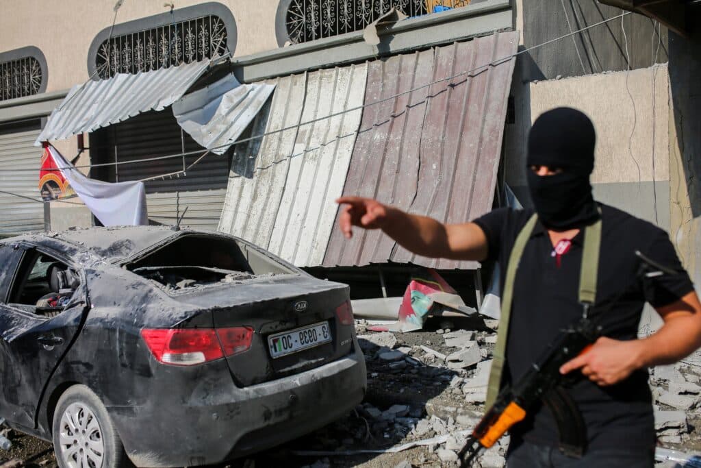 A masked armed man stands near damage after an Israeli strike in Gaza City.
