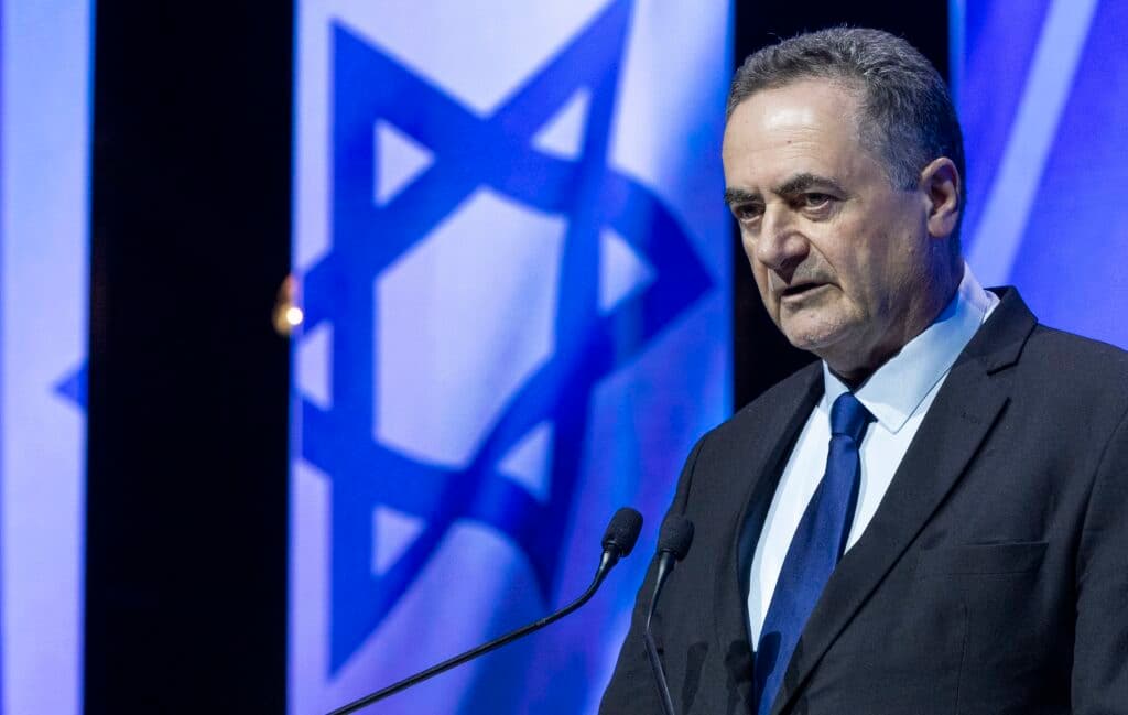 Defense Minister Israel Katz speaking at a podium with Israeli flags behind him