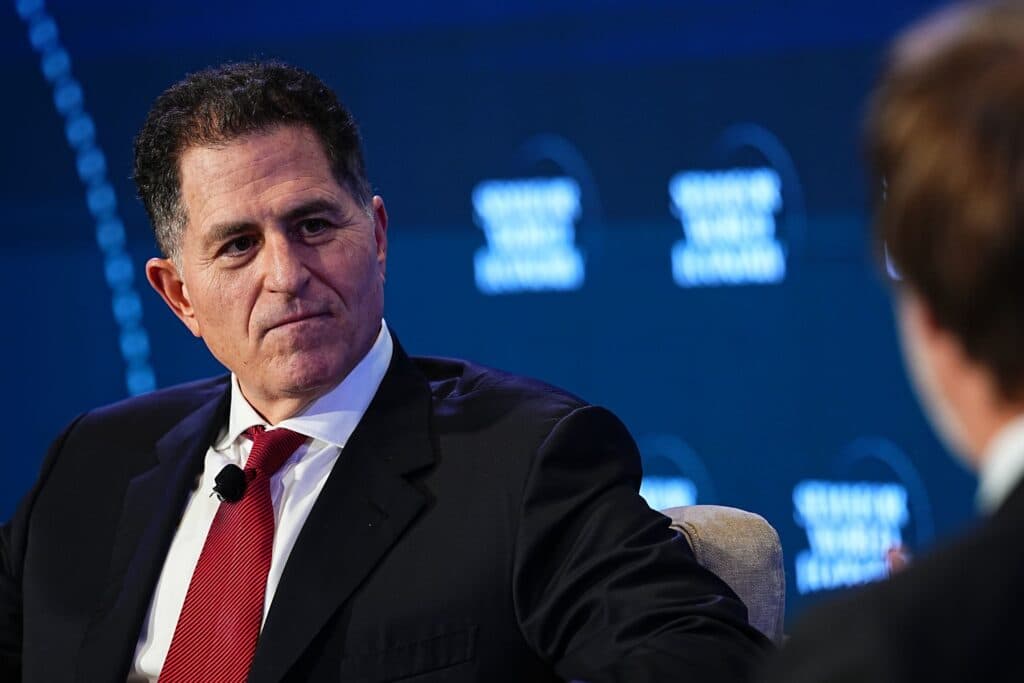 Michael Dell sits at an event with a blurred screen in the background.