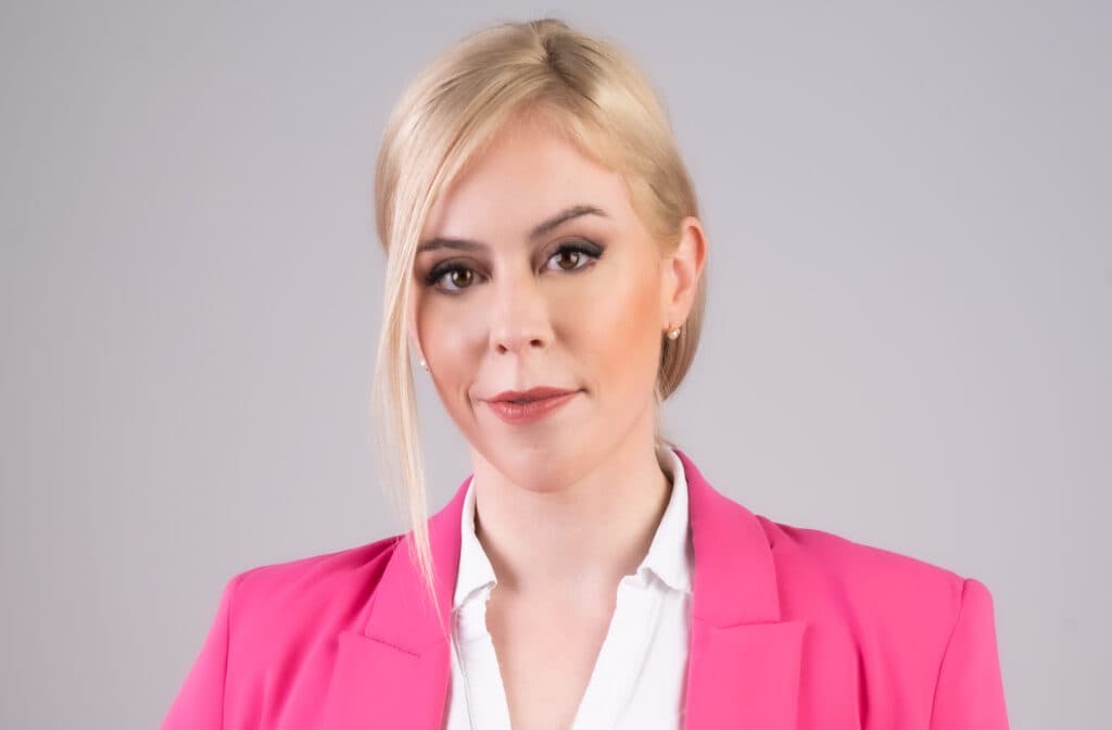Emily Schrader wearing a pink blazer against a gray background.