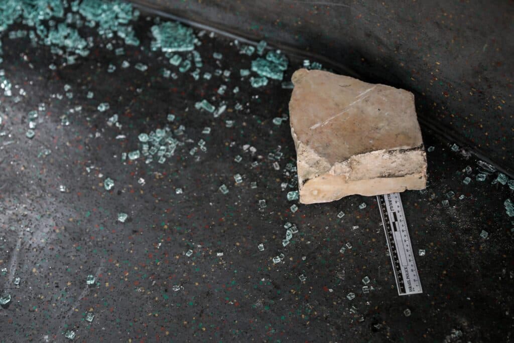 A large stone lies on shattered vehicle glass beside a police evidence ruler.