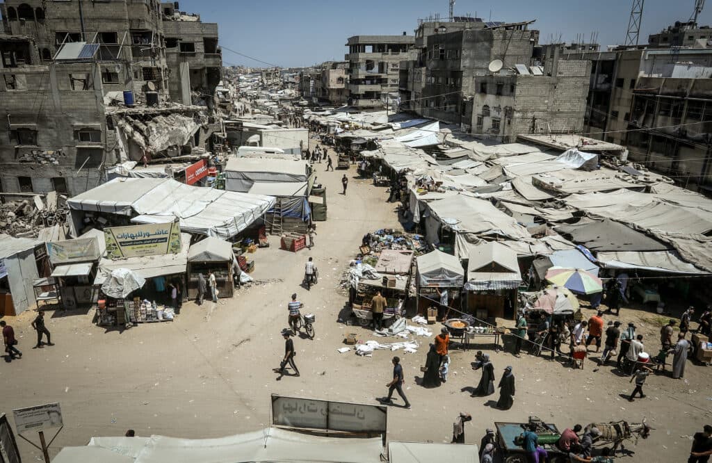 People walking through Khan Younis in southern Gaza amid damaged buildings and covered market stalls.