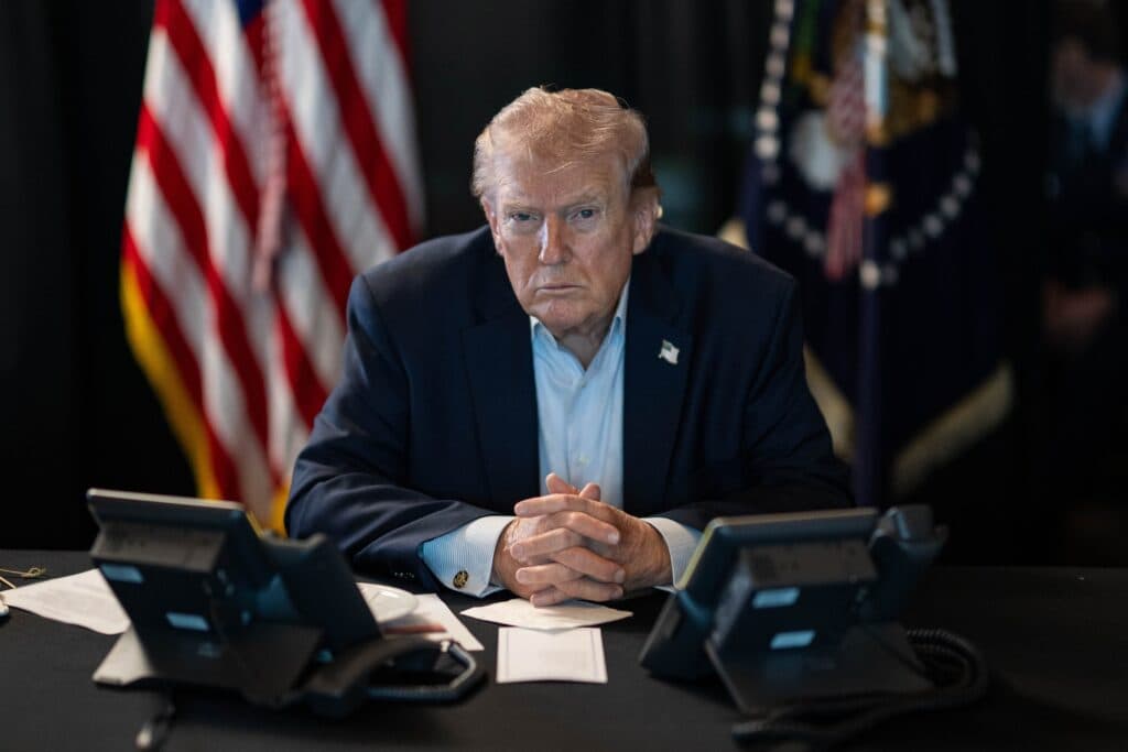 President Donald Trump seated at a table with American flags behind him.