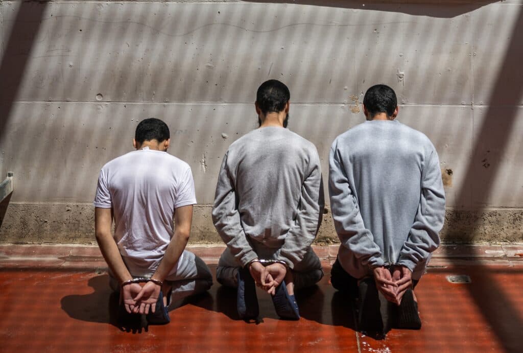 Three handcuffed detainees kneeling with their backs to the camera in an illustrative image.