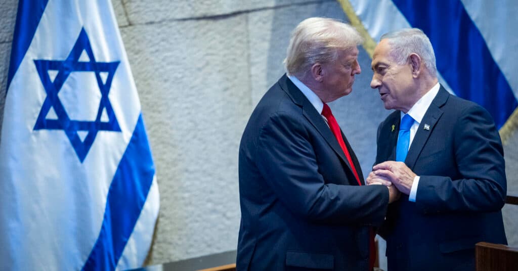 Donald Trump and Benjamin Netanyahu speak together at the Knesset in Jerusalem with Israeli flags behind them.