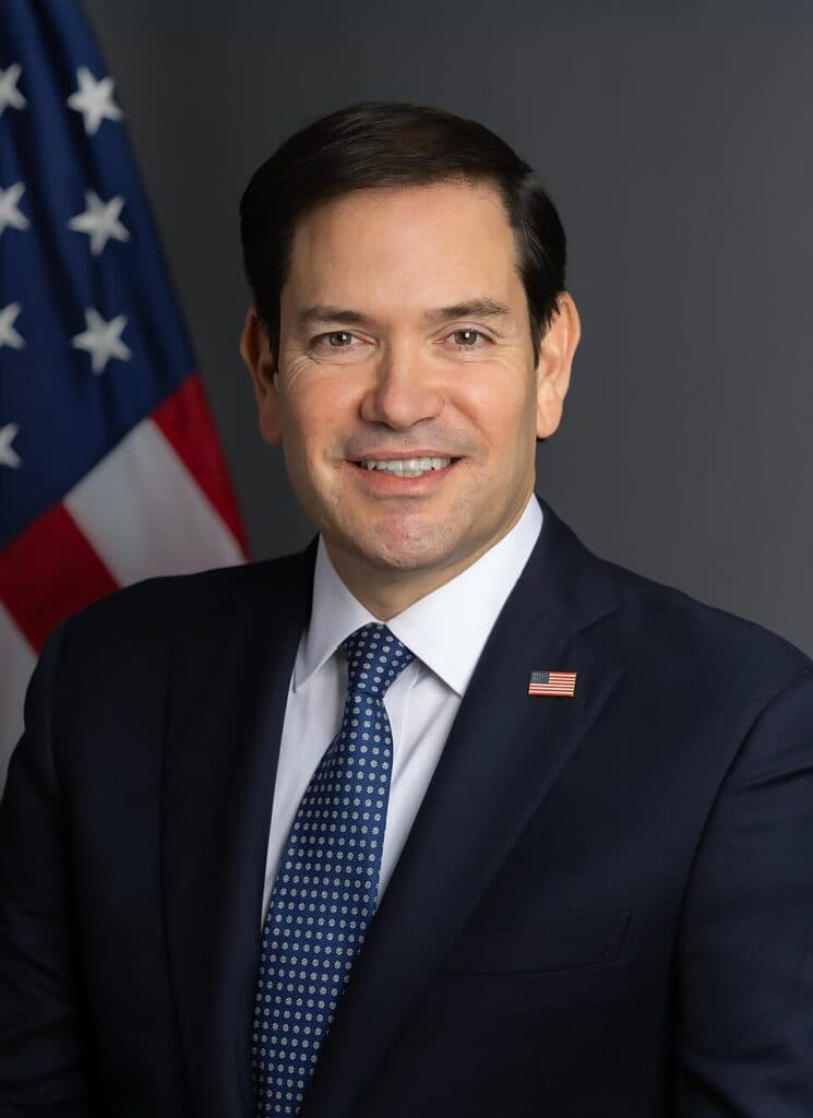 U.S. Secretary of State Marco Rubio posing for an official portrait with an American flag behind him.