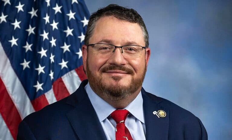 Rep. Randy Fine smiling in an official portrait with an American flag behind him.