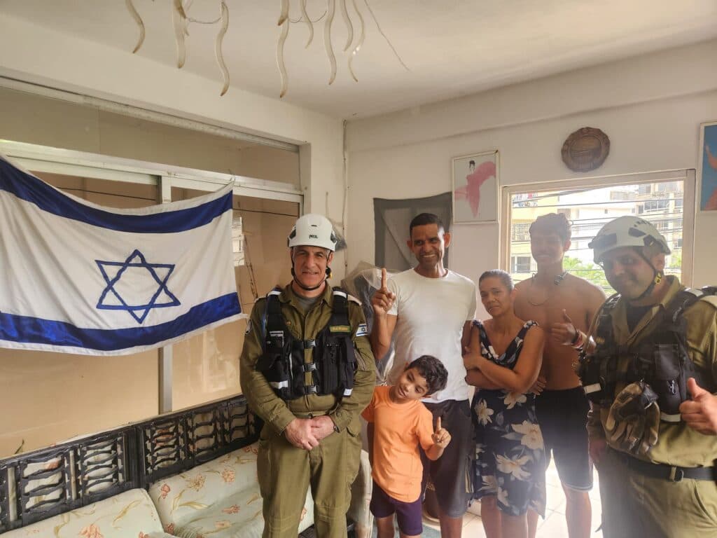 Israeli Home Front Command engineers standing with a Christian family beside an Israeli flag inside a home in Venezuela.