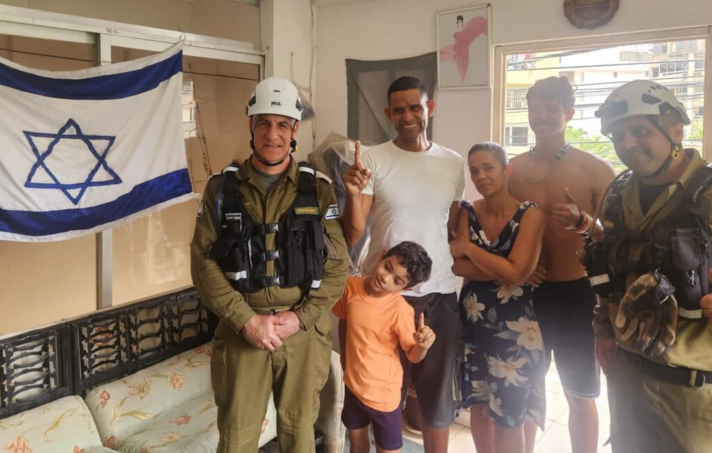 Israeli Home Front Command engineers standing with a Christian family beside an Israeli flag inside a home in Venezuela.