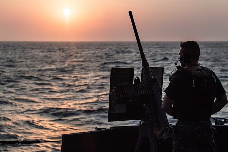 A U.S. Navy sailor mans a .50-caliber machine gun aboard a destroyer in the Bab al-Mandab Strait at sunset.