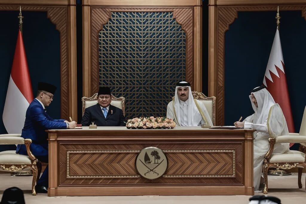 Qatar’s emir sits at a signing ceremony with Indonesian officials and Qatari flags visible behind them.