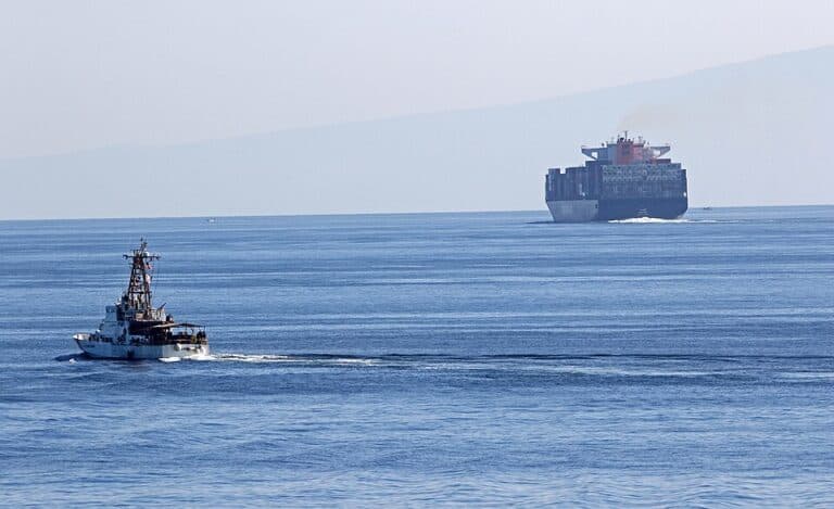 A U.S. Coast Guard cutter transits the Strait of Hormuz near a large cargo ship.