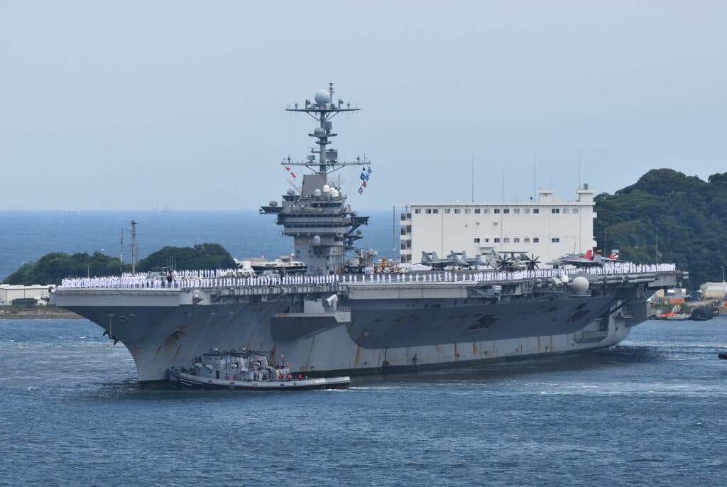 The USS George Washington aircraft carrier sailing at sea with sailors lined across the deck.
