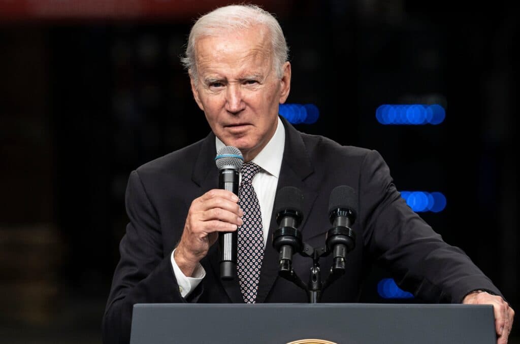Former President Joe Biden speaks at a podium while holding a microphone.