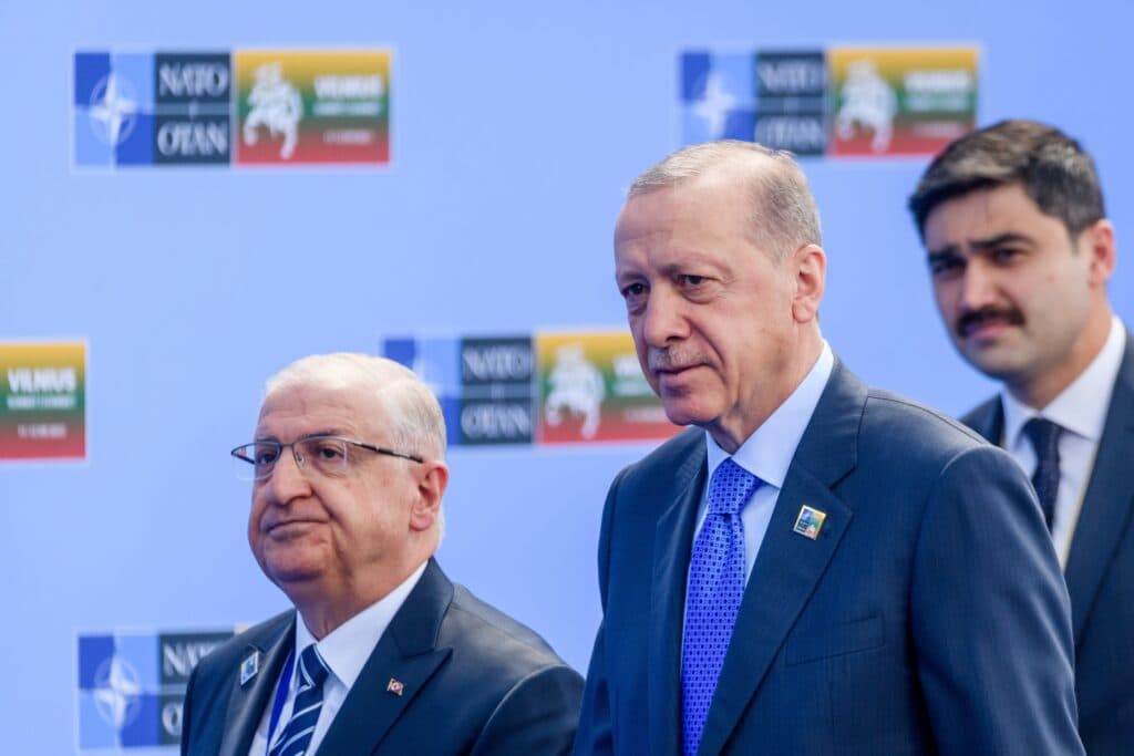 Turkish officials standing in front of NATO and summit signs.
