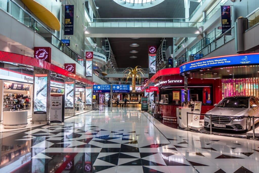 Interior of Dubai International Airport with duty-free shops, signs, and terminal walkways.