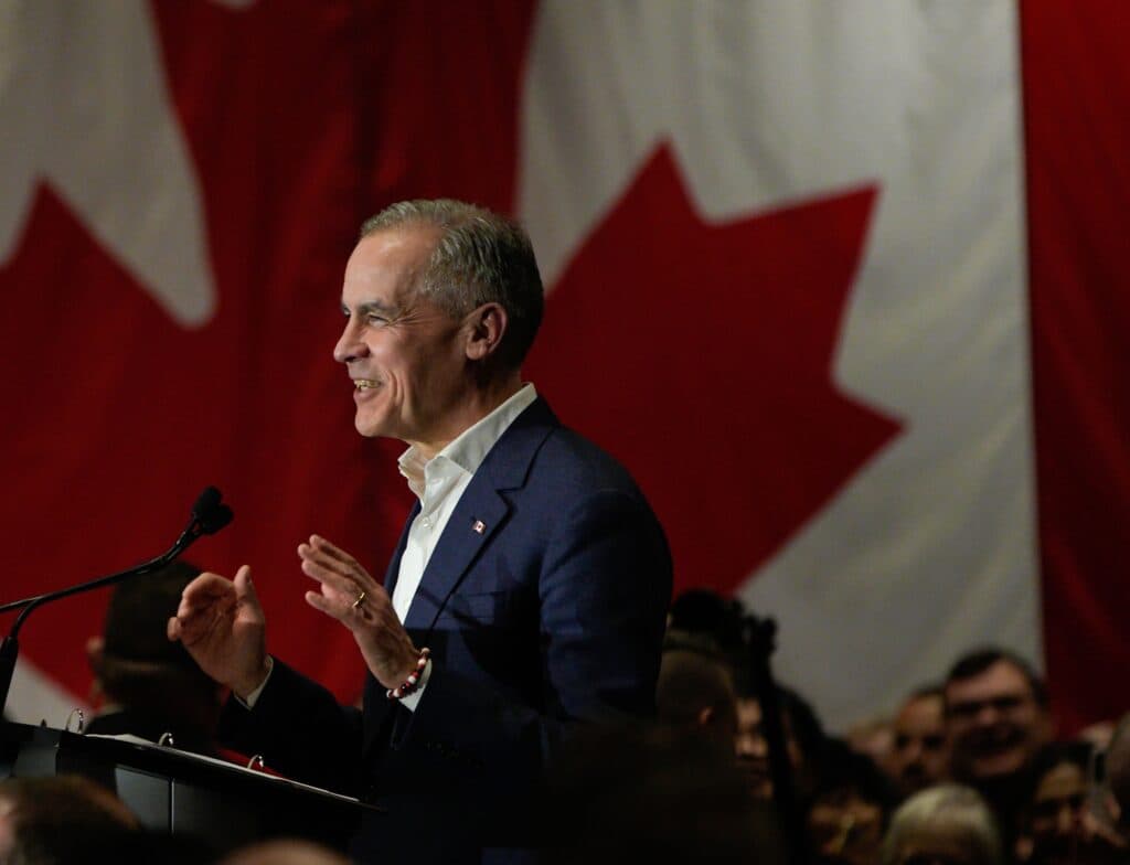 Canadian Prime Minister Mark Carney speaking at a podium in front of a large Canadian flag.