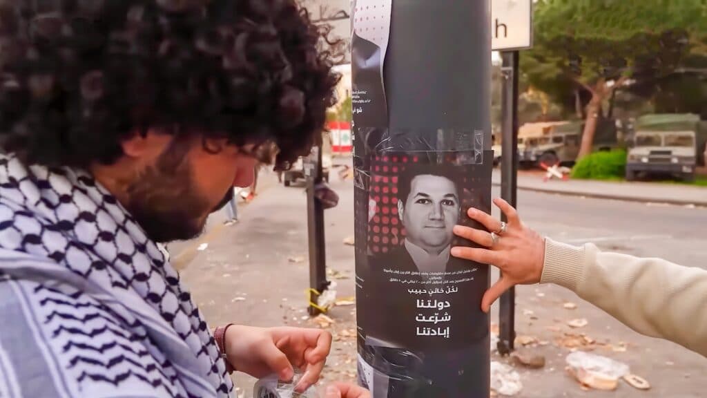 Hezbollah supporters in Beirut standing near a poster of Lebanese MP Nadim Gemayel.