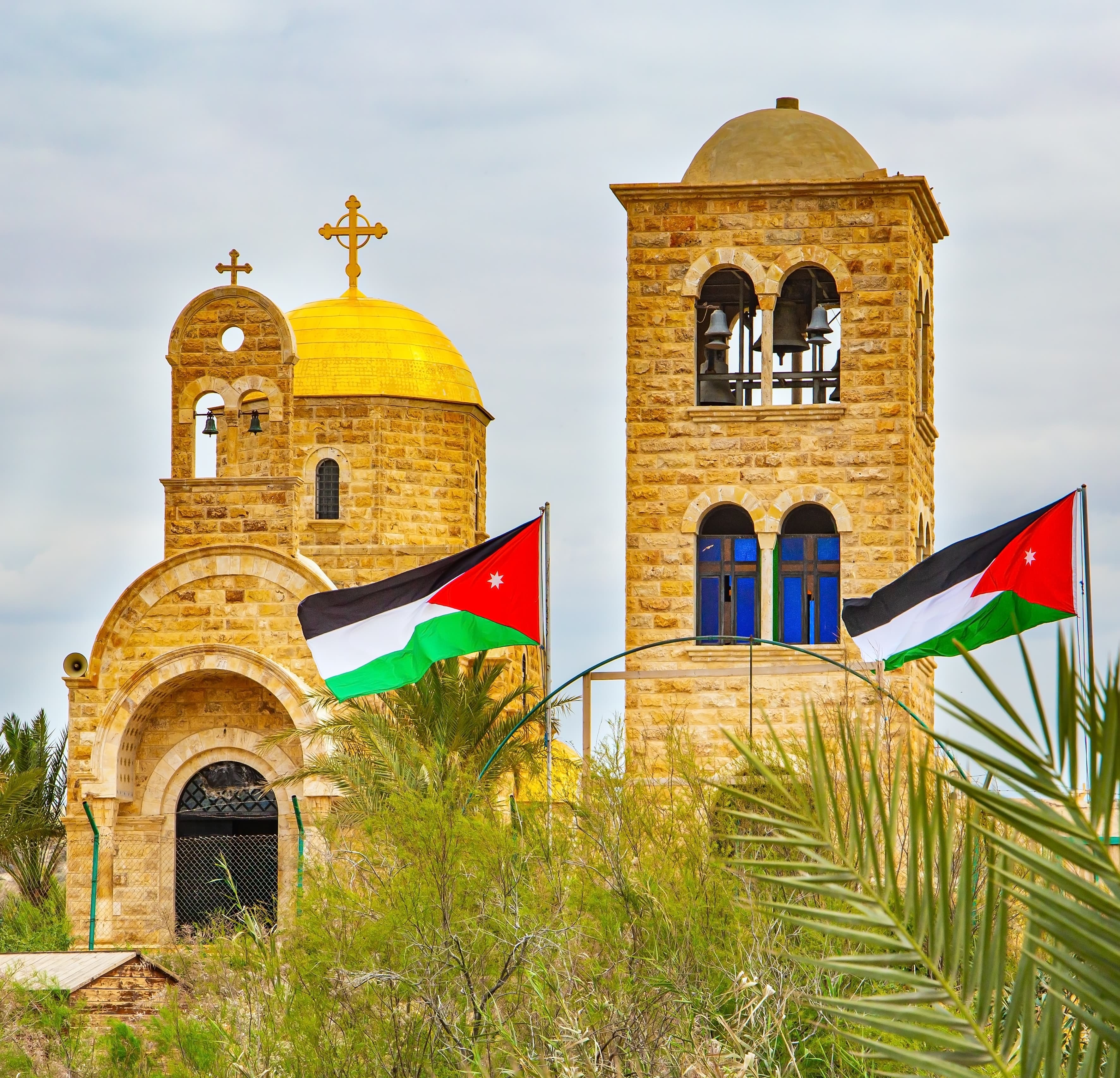 Greek Orthodox church near the Jordan River with Jordanian flags in the foreground.