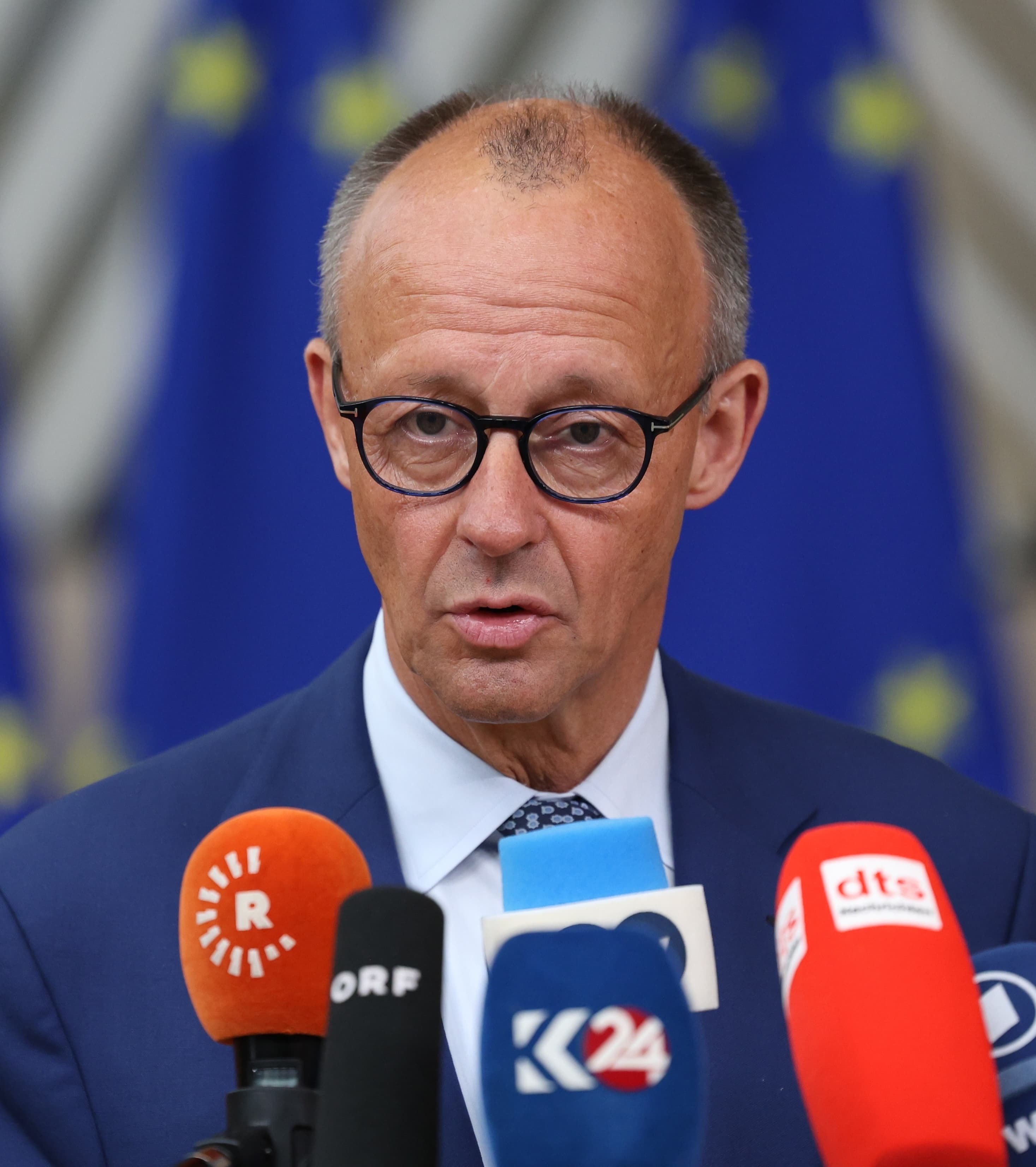 German Chancellor Friedrich Merz speaks to reporters in front of European Union flags.