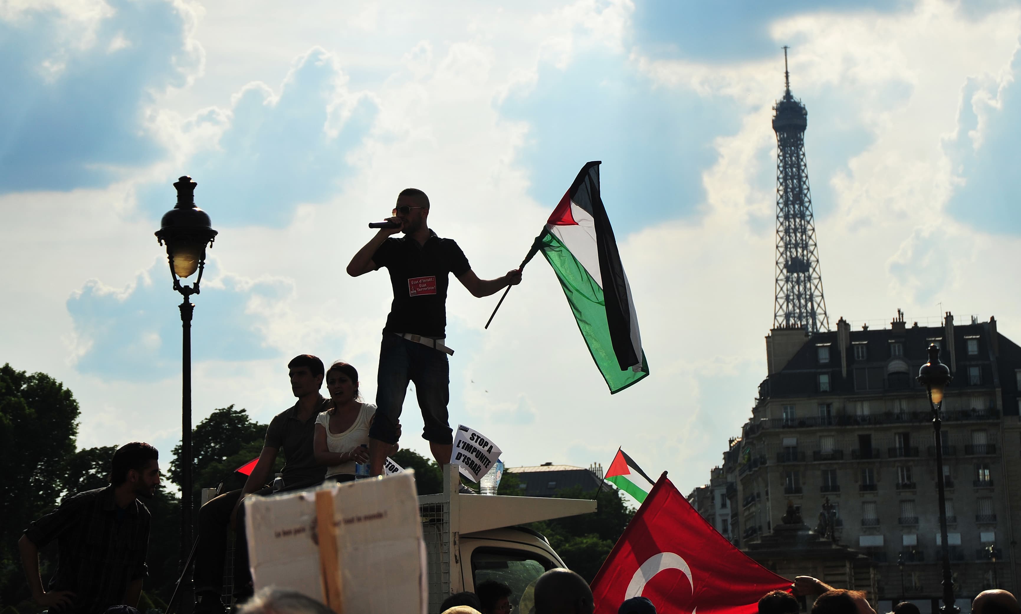 Protester holding a Palestinian flag during a riot in Paris with the Eiffel Tower in the background.
